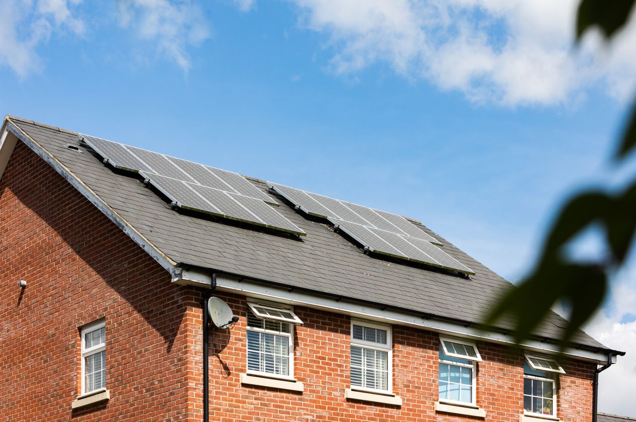 Brick house featuring solar panels on the roof under a clear blue sky, promoting sustainable energy.